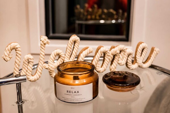 A candle labeled 'RELAX' on a glass table with a wooden wick holder and a decorative rope letter 'W' in the background.