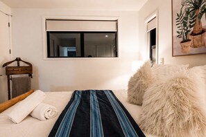 Un dormitorio con cama, ventana, cabecero de madera, planta colgante y almohada mullida.