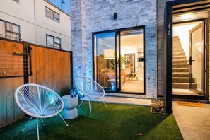 A modern house with a glass door entrance, a wooden fence, and two white chairs on the lawn.
