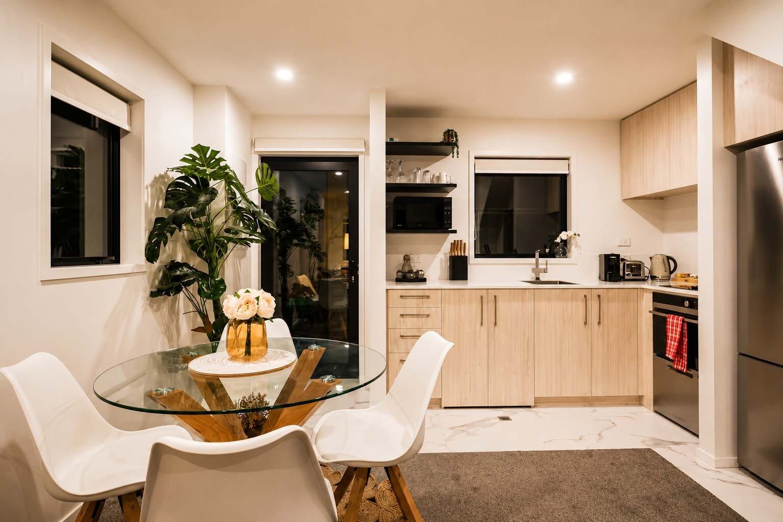 A modern kitchen with a glass dining table, white chairs, and wooden cabinets.