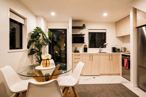 A modern kitchen with a glass dining table, white chairs, and wooden cabinets.