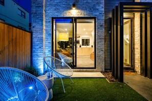 A modern house with a glass door entrance, a small patio with chairs, and a well-maintained lawn.
