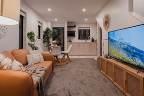 Een moderne woonkamer met een bank, een eettafel en een televisie op een houten dressoir.