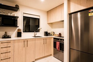 A modern kitchen with wooden cabinets, a stainless steel refrigerator, a window, and a sink.