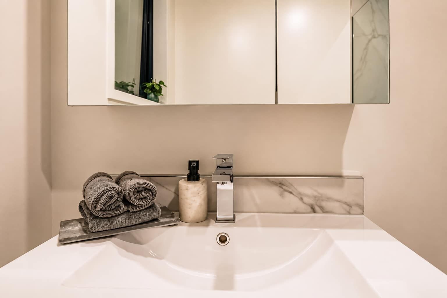 A bathroom with a white sink, a towel rack with folded towels, a soap dispenser, and a mirror above the sink.