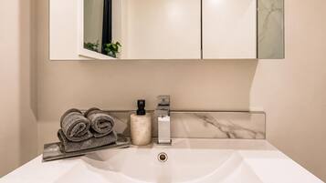 A bathroom with a white sink, a towel rack with folded towels, a soap dispenser, and a mirror above the sink.
