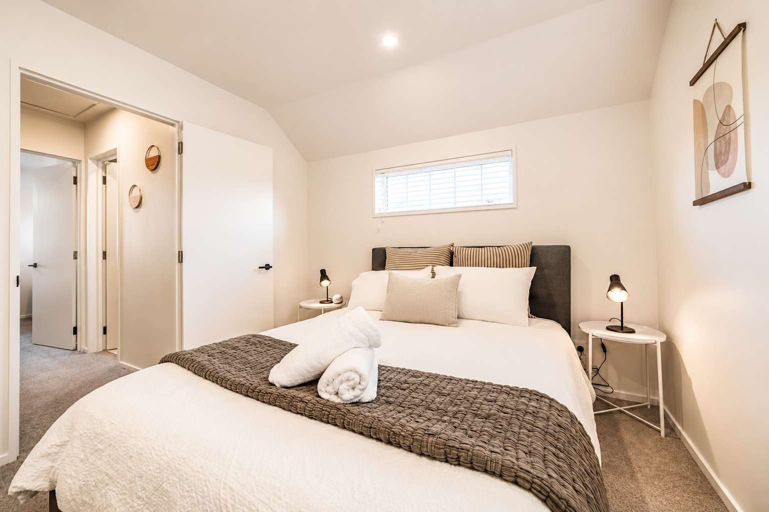 A bedroom with a bed, bedside tables, a window, and a door.