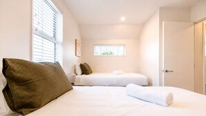 A hotel room with two beds, a window, a door, and a small window with blinds.