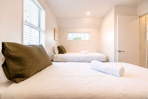 Ein Hotelzimmer mit zwei Betten, einem Fenster, einer Tür und einem kleinen Fenster mit Jalousien.