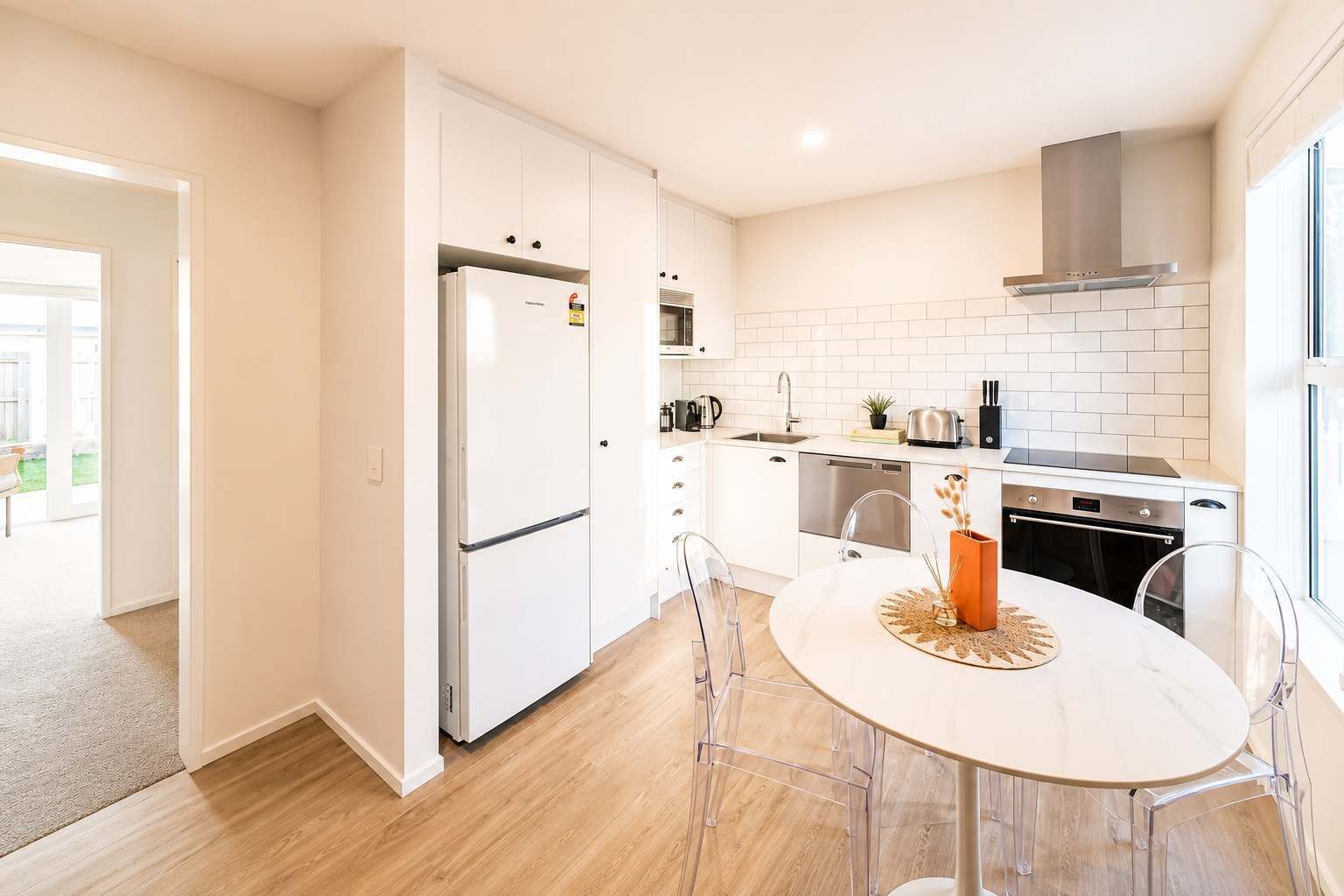 Una cocina moderna con armarios blancos, un refrigerador de acero inoxidable, horno empotrado y un comedor con mesa y sillas redondas.