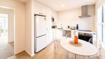 Una cocina moderna con armarios blancos, un refrigerador de acero inoxidable, horno empotrado y un comedor con mesa y sillas redondas.