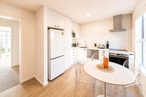 Una cocina moderna con armarios blancos, un refrigerador de acero inoxidable, horno empotrado y un comedor con mesa y sillas redondas.