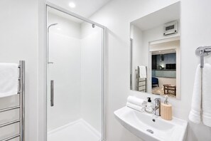 A modern bathroom with a glass shower enclosure, a white sink with a mirror, and a towel rack. - Fitzgerald City Base | 1BR + Patio + WiFi (Christchurch)