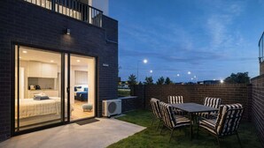 Un bâtiment moderne avec une entrée en verre donnant sur une chambre, un patio avec une table et des chaises, et un mur en briques.