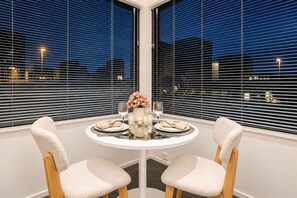 A dining area with a round table, two chairs, and a vase with flowers. - Fitzgerald City Base | 1BR + Patio + WiFi (Christchurch)