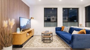 Un salon moderne avec un téléviseur, un mur recouvert de panneaux en bois, un canapé bleu et une petite table ronde.