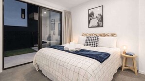 Une chambre à coucher avec un lit, une table de chevet avec une lampe, un tableau encadré au mur et une porte-fenêtre coulissante donnant sur un espace extérieur.