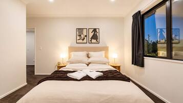 Quarto de hotel com uma cama grande, duas luminárias de cabeceira, uma janela com cortinas e duas imagens emolduradas na parede.