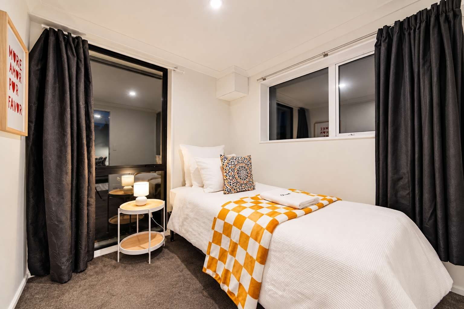 A hotel room with a bed, a small table with a lamp, a window, and a door leading to a bathroom.
