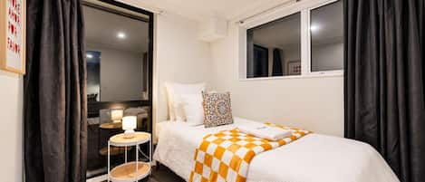 Habitación de hotel con cama, una mesita de noche con lámpara, ventana y puerta que da a un baño.