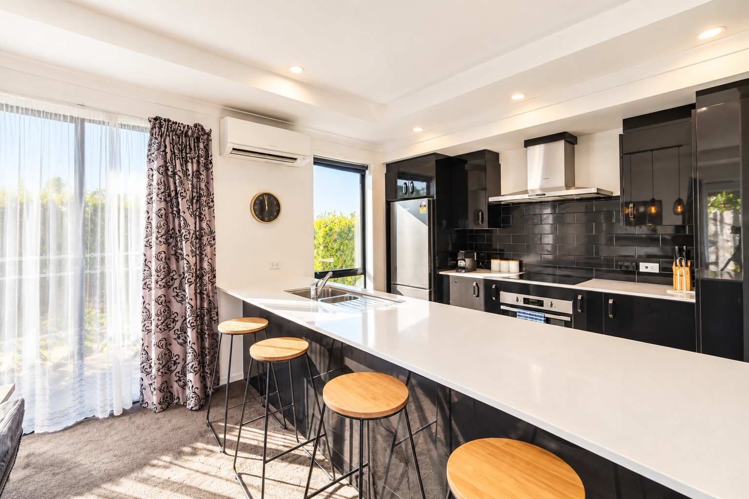 Una cocina moderna con una isla grande, taburetes de bar y vistas a zonas verdes.