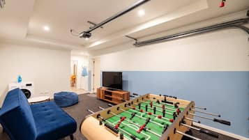 Una habitación con mesa de fútbol, sofá, televisor y lavadora.