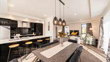 A modern kitchen with black cabinets, a central island with stools, and a dining area with a table and chairs.