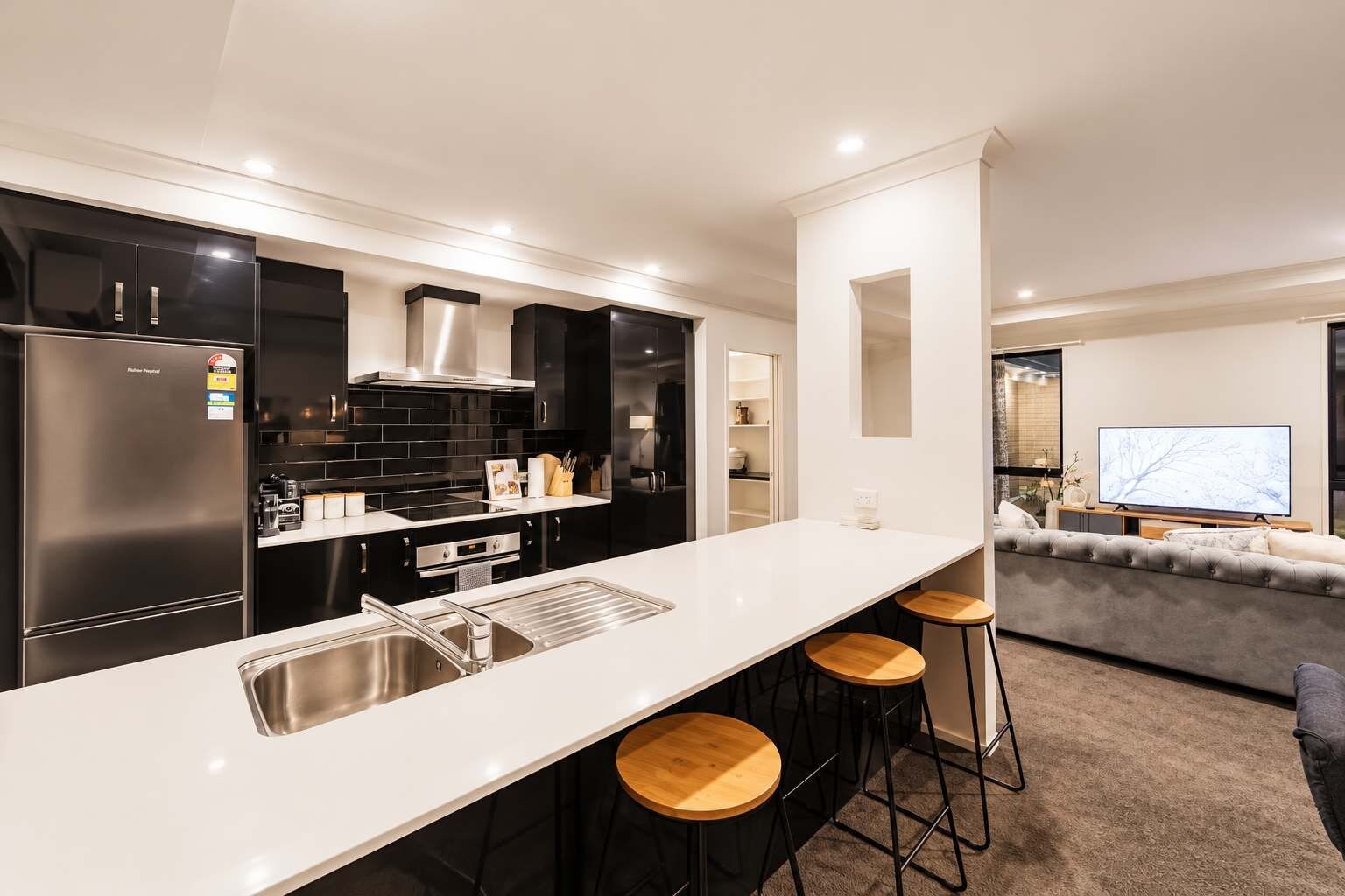 Una cocina moderna con una isla central, taburetes de bar y un área de comedor con sofá y televisor.