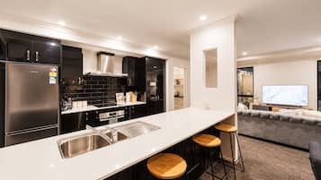 A modern kitchen with a central island, bar stools, and a dining area with a sofa and TV.