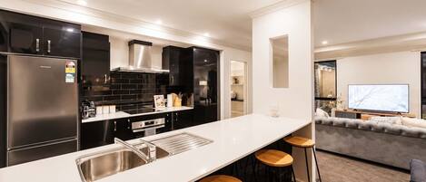 Una cocina moderna con una isla central, taburetes de bar y un área de comedor con sofá y televisor.