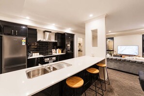 A modern kitchen with a central island, bar stools, and a dining area with a sofa and TV.