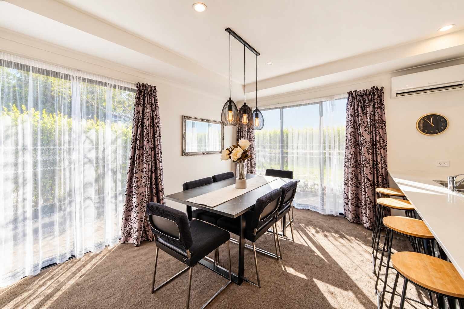 A modern dining area with a long table, chairs, and pendant lighting.