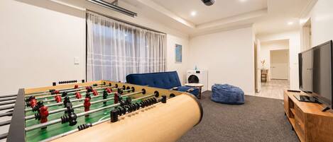 A room with a foosball table, a blue sofa, a television, and a projector on the ceiling.