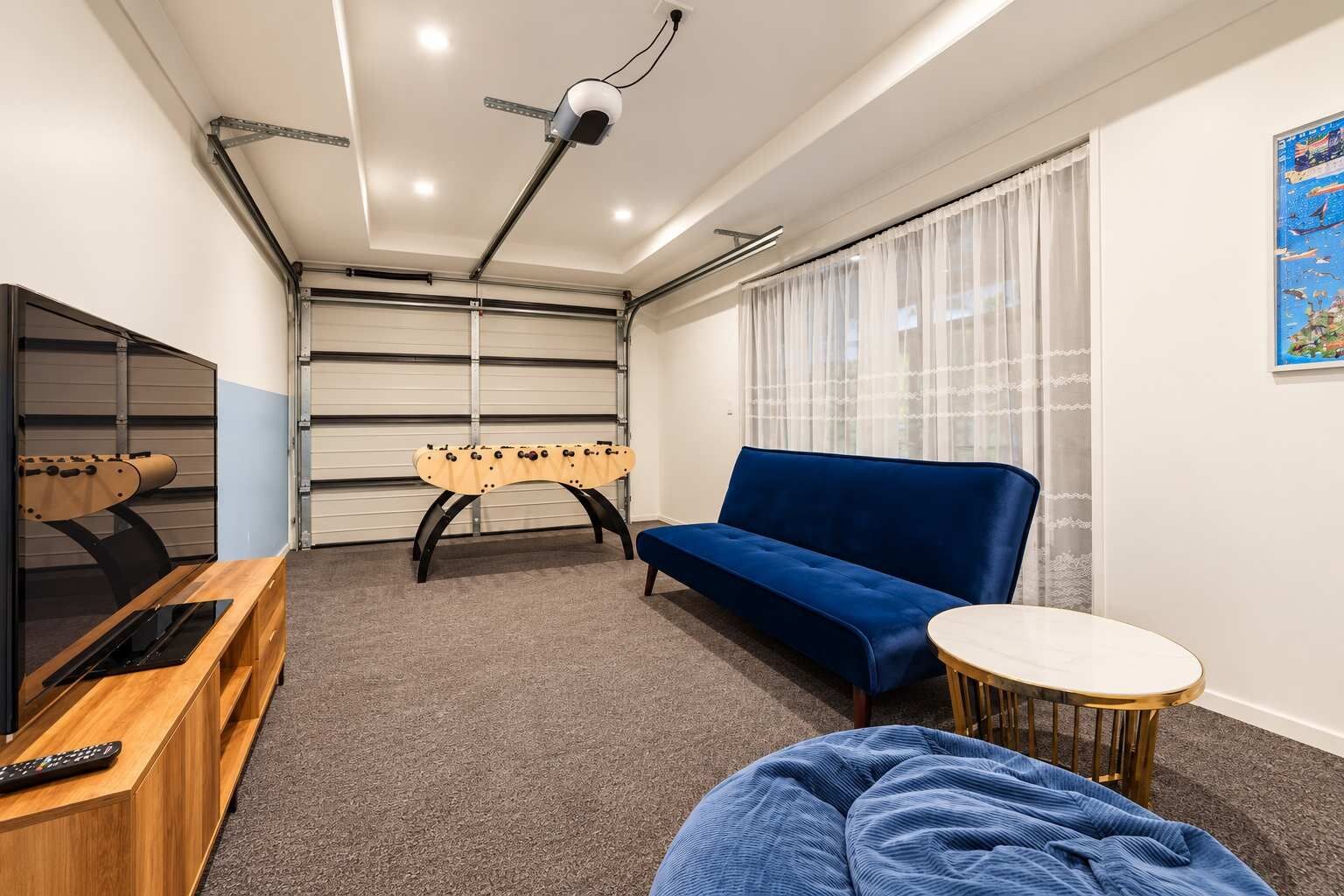 A room with a blue sofa, a foosball table, a TV, and a small round table.