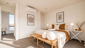 Un dormitorio moderno con una cama grande, dos aires acondicionados empotrados y dos obras de arte enmarcadas.
