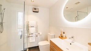 Une salle de bain moderne avec une douche à parois de verre, des toilettes, un lavabo avec un miroir et un porte-serviettes.