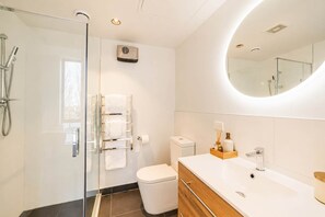 A modern bathroom with a glass shower enclosure, a toilet, a sink with a mirror, and a towel rack.