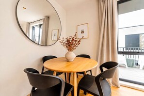 A round wooden table with a vase of dried flowers, surrounded by black chairs, in a room with a large mirror and framed pictures on the wall.