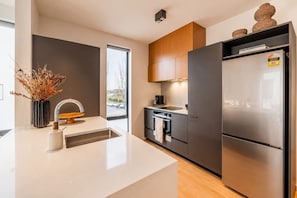 A modern kitchen with a central island, stainless steel appliances, and a view of the street outside. - Cambridge Terrace | 2BR | Parking + Balcony | CBD (Christchurch)