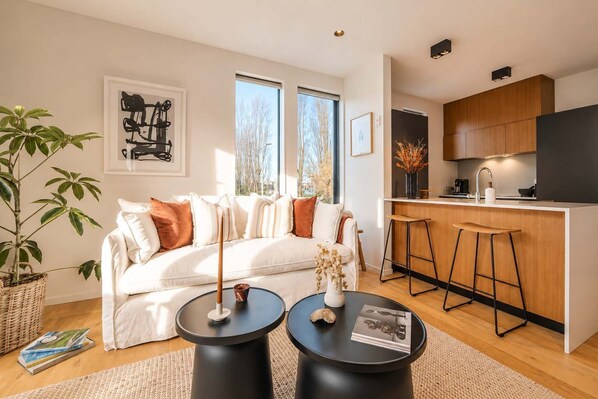A modern living room with a sofa, two round tables, and a kitchen area with a bar stool.