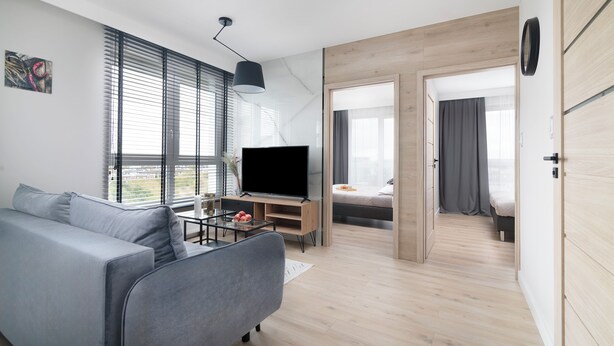A modern living room with a grey sofa, a flat-screen TV, and a wooden floor. - EASY RENT Apartments- Kompozytorów 7 (Lublin)