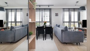 A modern living room with two grey sofas, a dining table with chairs, and large windows with blinds. - EASY RENT Apartments- Kompozytorów 7 (Lublin)