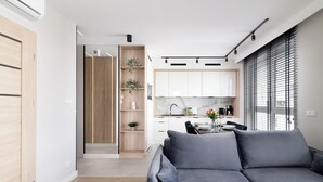 A modern living room with a grey sofa, wooden flooring, and a kitchen area with white cabinets and a black countertop. - EASY RENT Apartments- Kompozytorów 7 (Lublin)