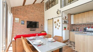 A dining area with a brick wall, a television, and a kitchen with wooden cabinets.
