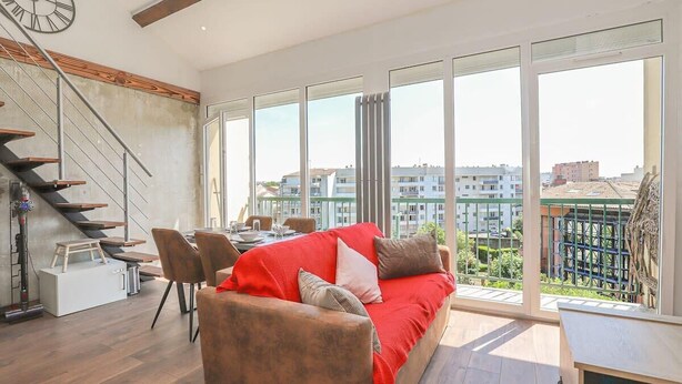 A modern living room with a red sofa, a dining area, and a staircase.