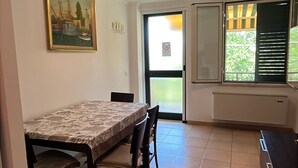 Una cocina con una mesa de comedor, sillas, un cuadro en la pared, una ventana con persianas y una lámpara en el techo.