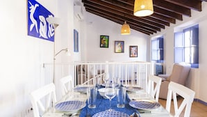 Comedor con una mesa de vidrio dispuesta para seis personas, sillas blancas y un mantel azul.