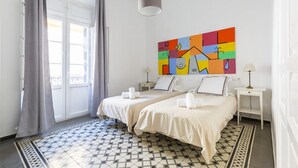 Habitación de hotel con dos camas, un cuadro abstracto colorido en la pared, suelo estampado y una ventana con cortinas.