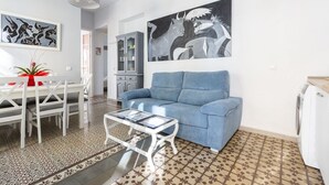 Uma sala de estar com um sofá azul, uma mesa de jantar com cadeiras, uma mesa de centro e duas pinturas abstratas nas paredes.