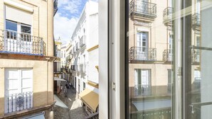 Uma rua estreita com edifícios de ambos os lados, com varandas e grades de metal, e um caminho de calçada.